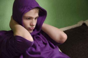 Depressed teenager with arms around his neck and hood on head