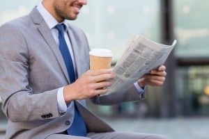 business, news, break and people and concept - close up of smiling businessman reading newspaper and drinking coffee from paper cup over office building