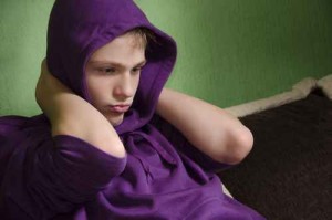Depressed teenager with arms around his neck and hood on head